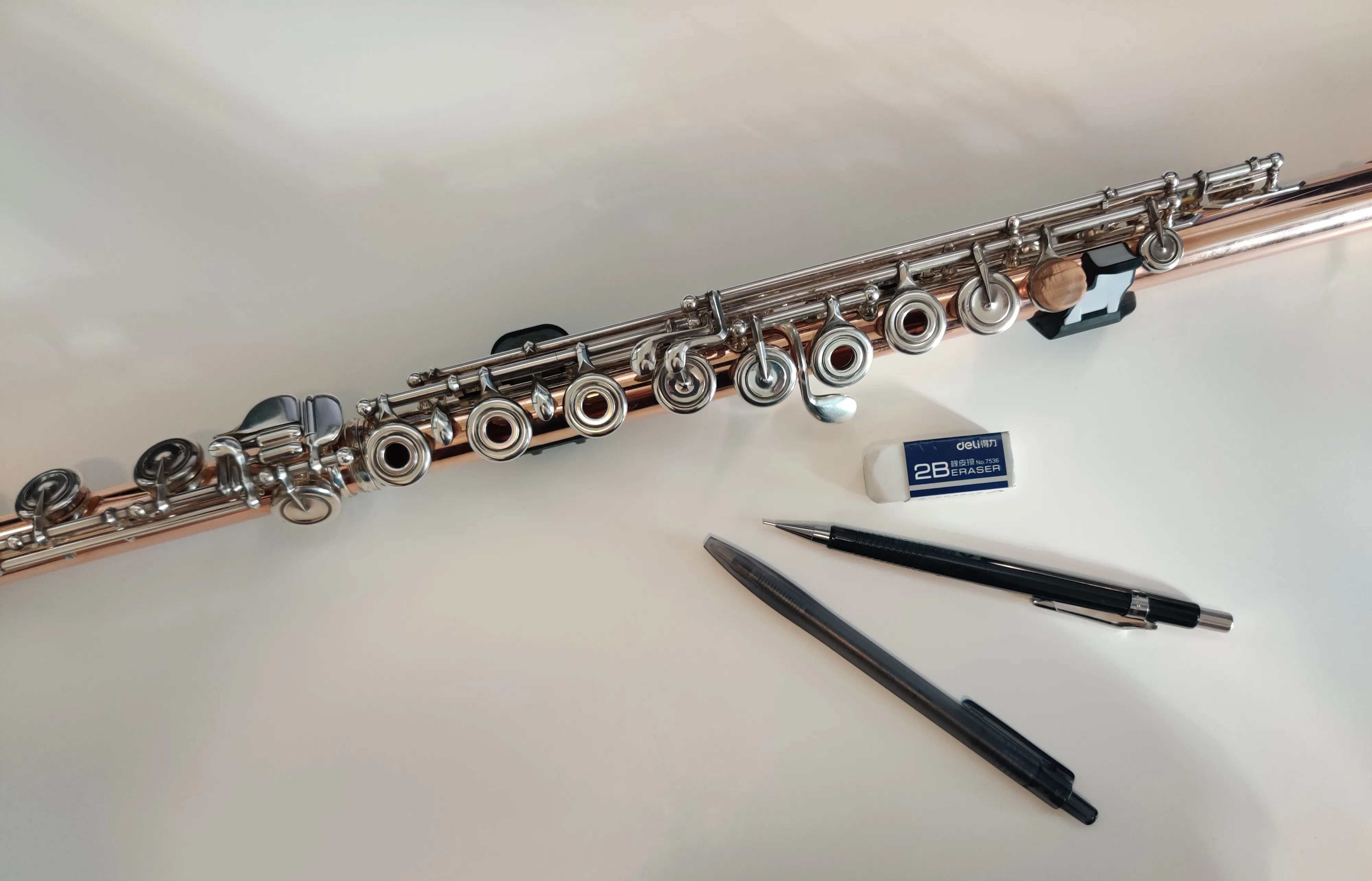 A rose gold flute surrounded by pencils on a white desk